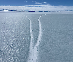 A crack that has refrozen into the sea ice splits into two and extends into the distance towards a number of icebergs