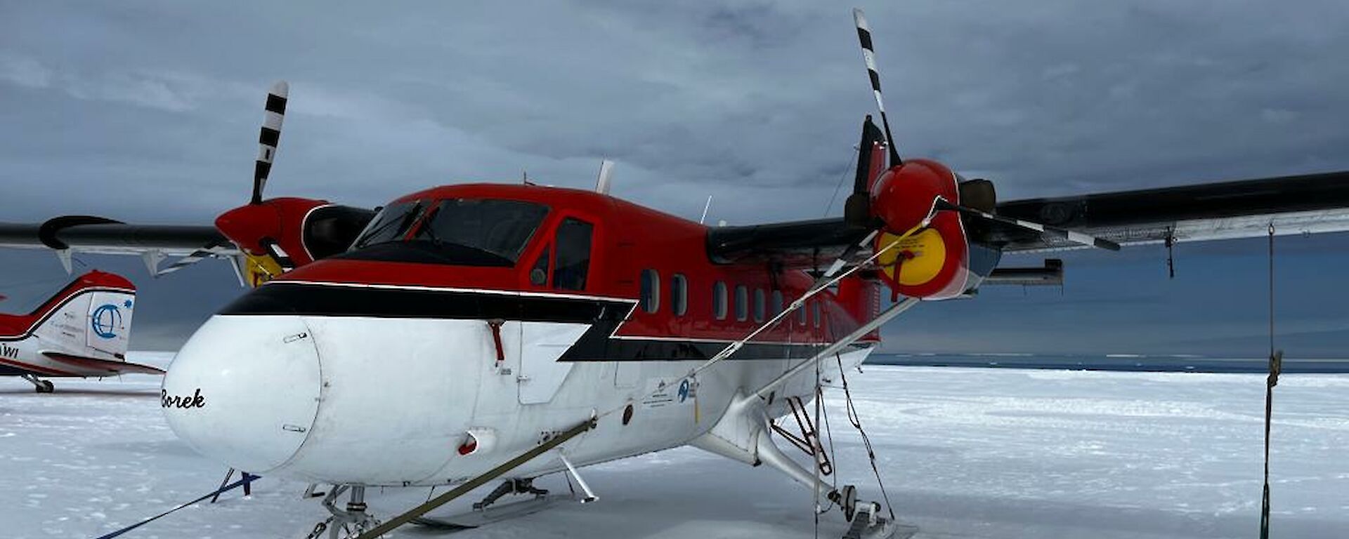 Red and white twin otter aircraft parked on snow