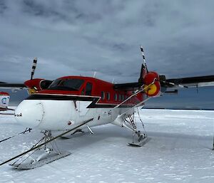 Red and white twin otter aircraft parked on snow