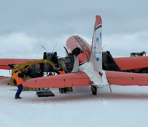 An orange plane being loaded with cargo as it sits on the ice