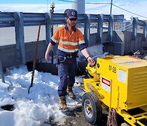 A man is next to a yellow heating unit. Next to him is a pile of snow with a shovel placed in it