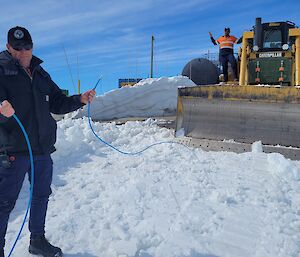 A man is holding a piece of cable that appears to have been cut in two. Behind him is a excavator with a man standing on the side