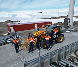 Four men are around a loader which is holdinga large drum of fibre optic cable. In the background are large icebergs