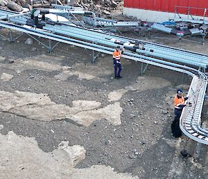 Two men are laying fibre optic cable into metal cable tray that runs over a rocky landscape