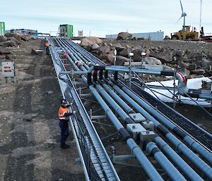 Two men are laying fibre optic cable into metal cable tray that runs over a rocky landscape