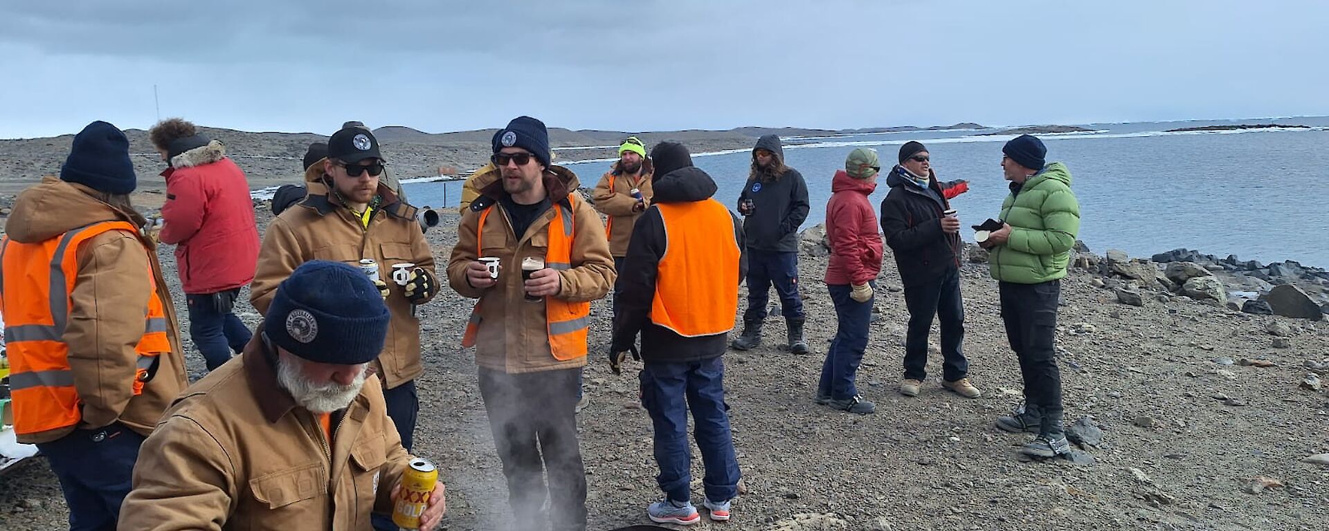 A group of people gather around the shore at Club Lake while one person cooks on a BBQ