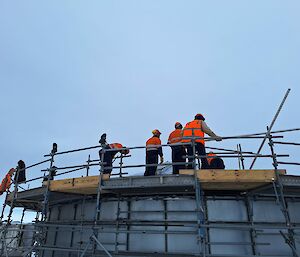 Five people in high vis stand on top of a water tower with scaffolding surrounding the tower