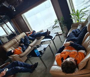 Three people stretched out, asleep across two couches