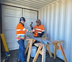 Two men in high vis working on tools smiling. One is using a hammer and the other is using the drill.