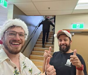Two men in Santa hats smiling at the camera