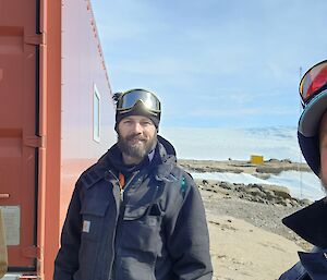 Three carpenters standing beside a freshly painted Red shipping container with the Ice of the Plateau in the background.