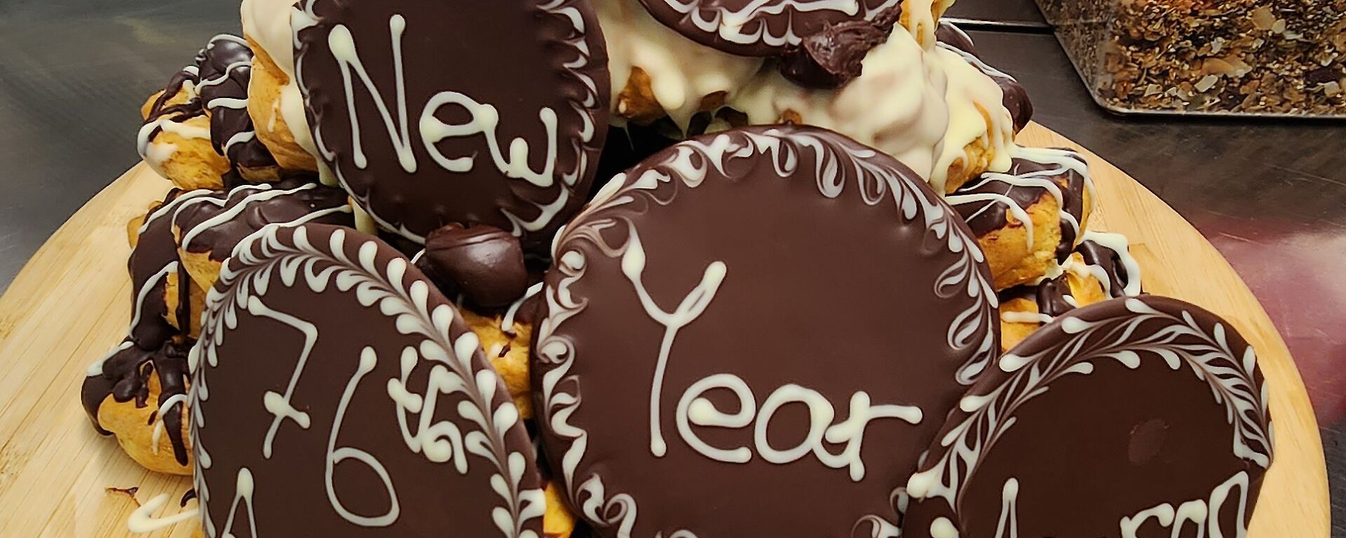 Happy New Year 76th ANARE, Mawson written on chocolate cookies, stacked on a small mountain of profiteroles, smothered in chocolate and cream.
