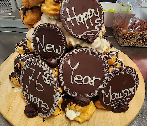 Happy New Year 76th ANARE, Mawson written on chocolate cookies, stacked on a small mountain of profiteroles, smothered in chocolate and cream.