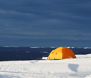 Orange tent set up on ice near blue ocean