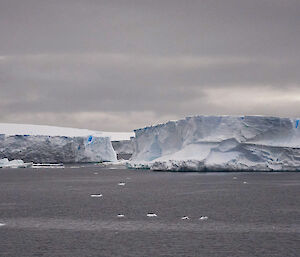 Two large white and blue icebergs floating on a grey ocean.