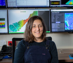 A woman sitting in front of computer monitors featuring colourful acoustic maps.