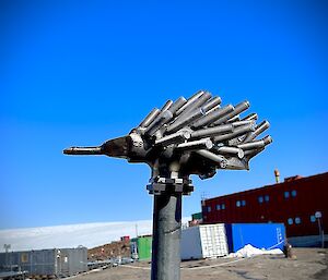 Metal art sculpture of an Echidna with blue sky behind.