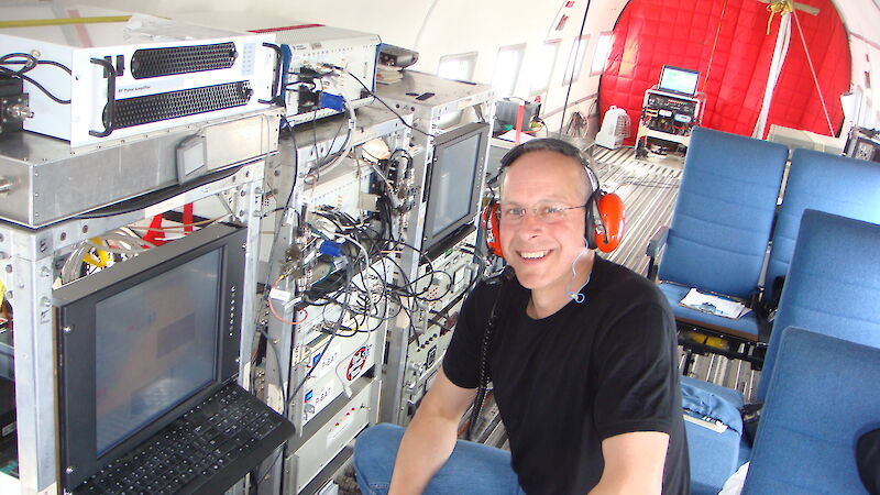 Expeditioner with headphones on sitting near a bank of scientific equipment