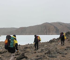 Three people with backpacks walk across a rocky hillside.