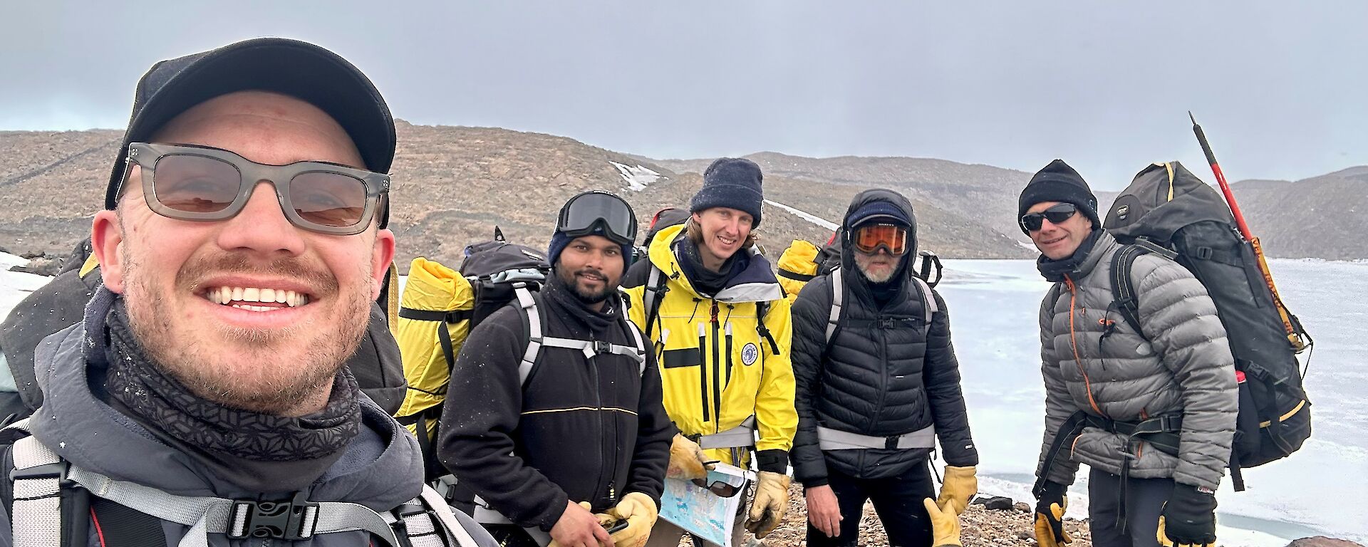 Five hikers stand on a rocky isthmus.