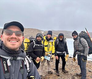 Five hikers stand on a rocky isthmus.