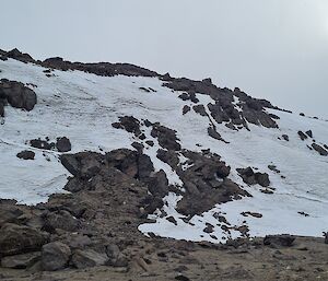 Snow covered rock face tapering left to right with pale sun in top right on overcast day on route to Brooks Hut.