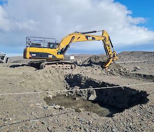 Large yellow digger on tracks with deep hole in foreground.