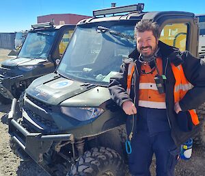 Two Polaris ATVs on left side with Author in High visibility workwear leaning on vehicle. Field Store Building in background.