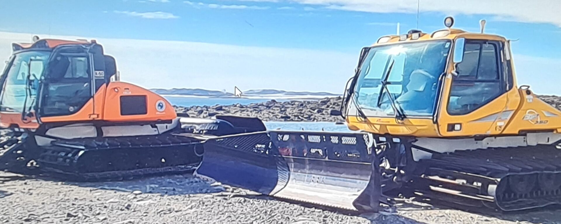 two wide tracked dozer blade equipped snow plough vehilcles with wide enclosed cabs one orange one yellow.