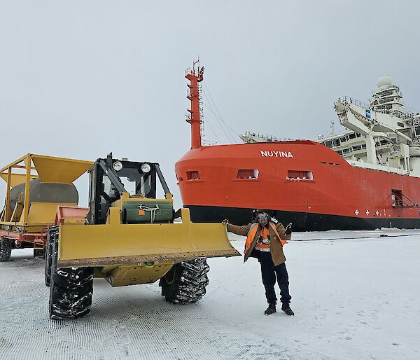 Expeditioner standing beside a tractor on the sea ice with Nuyina in the background