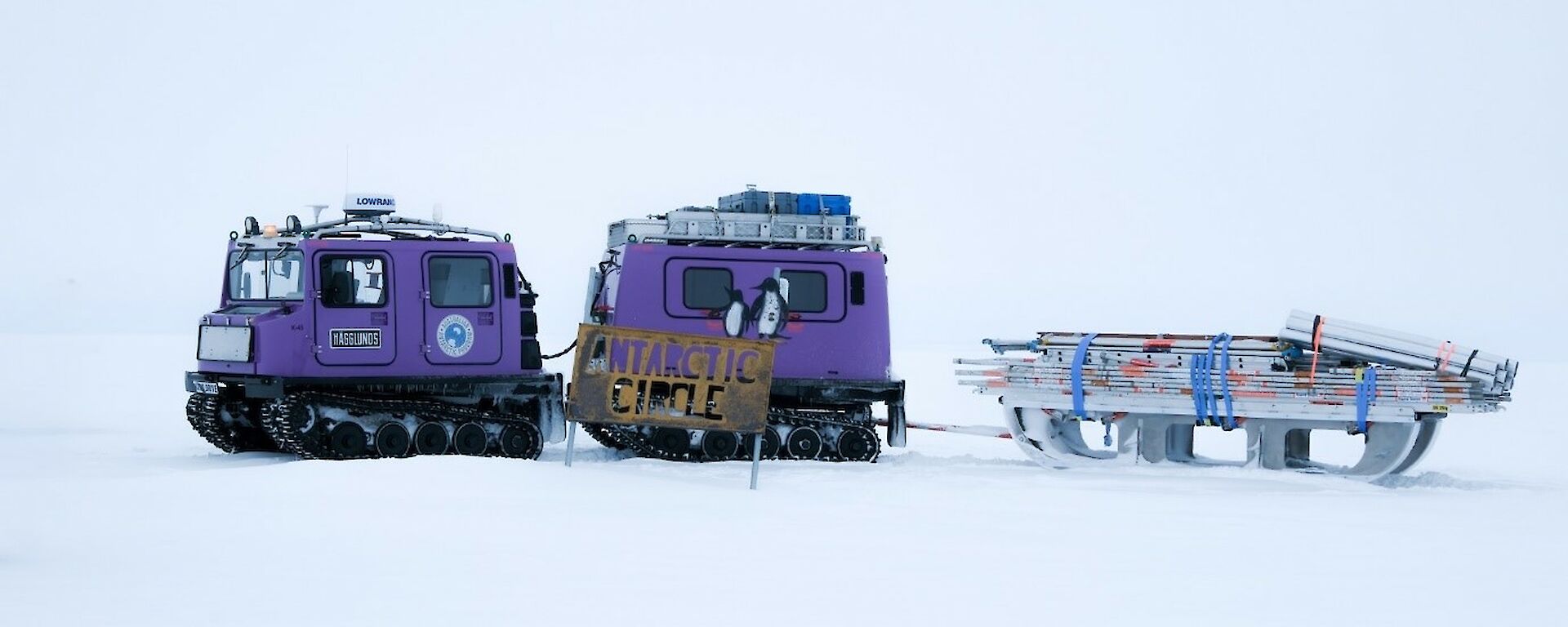 Hagglund over snow vehicle towing scaffolding equipment with white snow foreground and background.