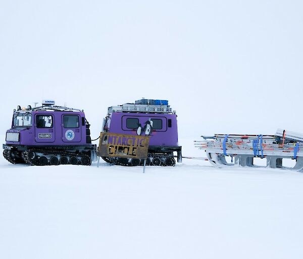 Hagglund over snow vehicle towing scaffolding equipment with white snow foreground and background.