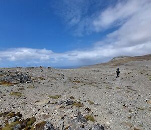 A pebbly hillside with a person in the distance and blue skies overhead.