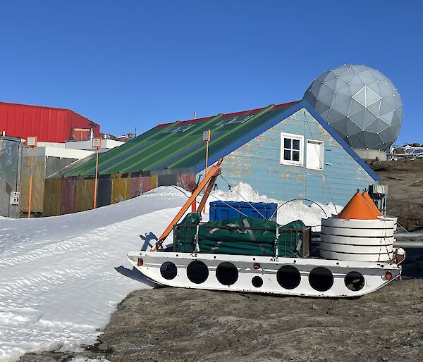 A green and blue hut in the foreground with a red shed in the background.