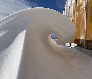 A frozen snow wave up against a yellow building.