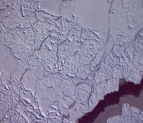 Aerial view of sea ice with cracks revealing a dark ocean beneath