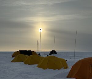 A row of five yellow tents on snow with the sun setting in the background