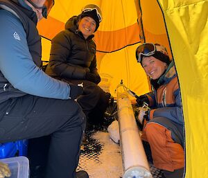 three expeditioners in a tent examining an ice core sample