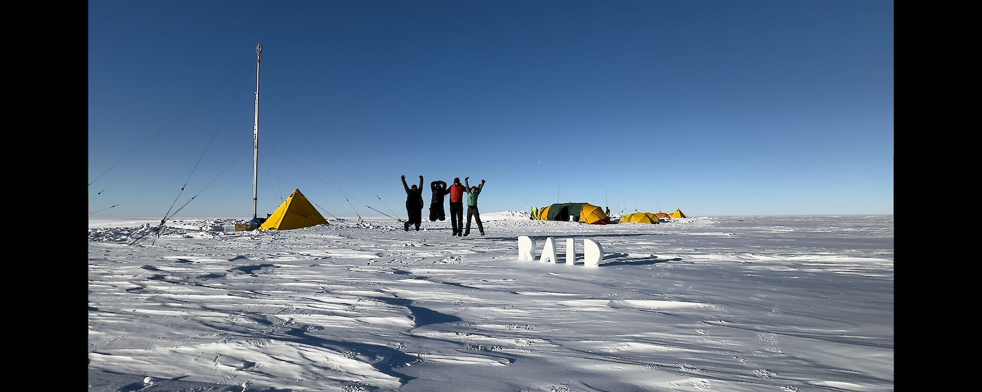 Four expeditioners jumping in the air in front of their camp site and ice drill