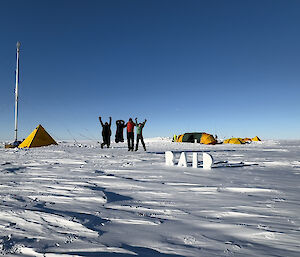 Four expeditioners jumping in the air in front of their camp site and ice drill