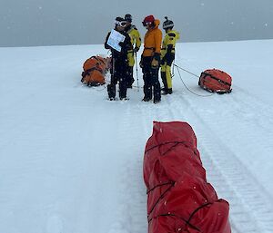 Four expeditioners with sleds standing in the snow navigating via map