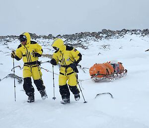 two expeditioners hauling a wooden sled in high winds and snow