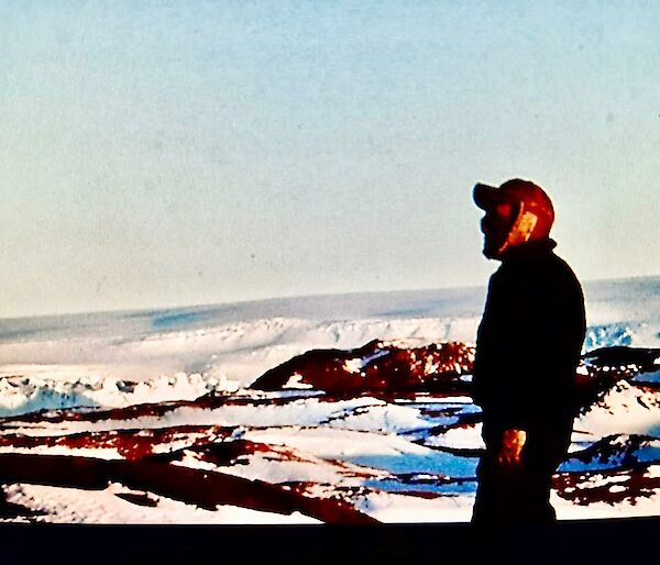 A man stands in the foreground of an icy landscape with a brown woolly cap on.