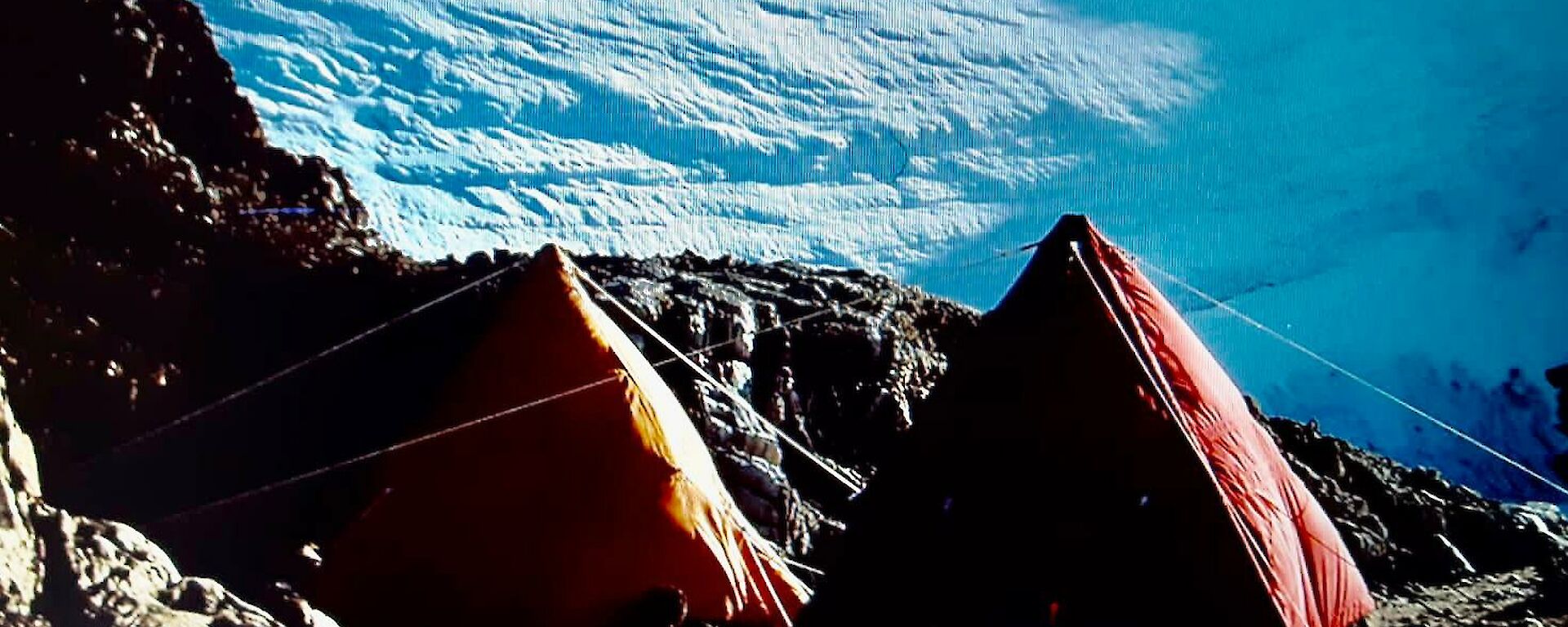 Two pyramid's pitched on a rocky ledge in front of an ice shelf.