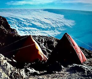 Two pyramid's pitched on a rocky ledge in front of an ice shelf.