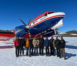A group of ten people stand in front of a plane on the ice.