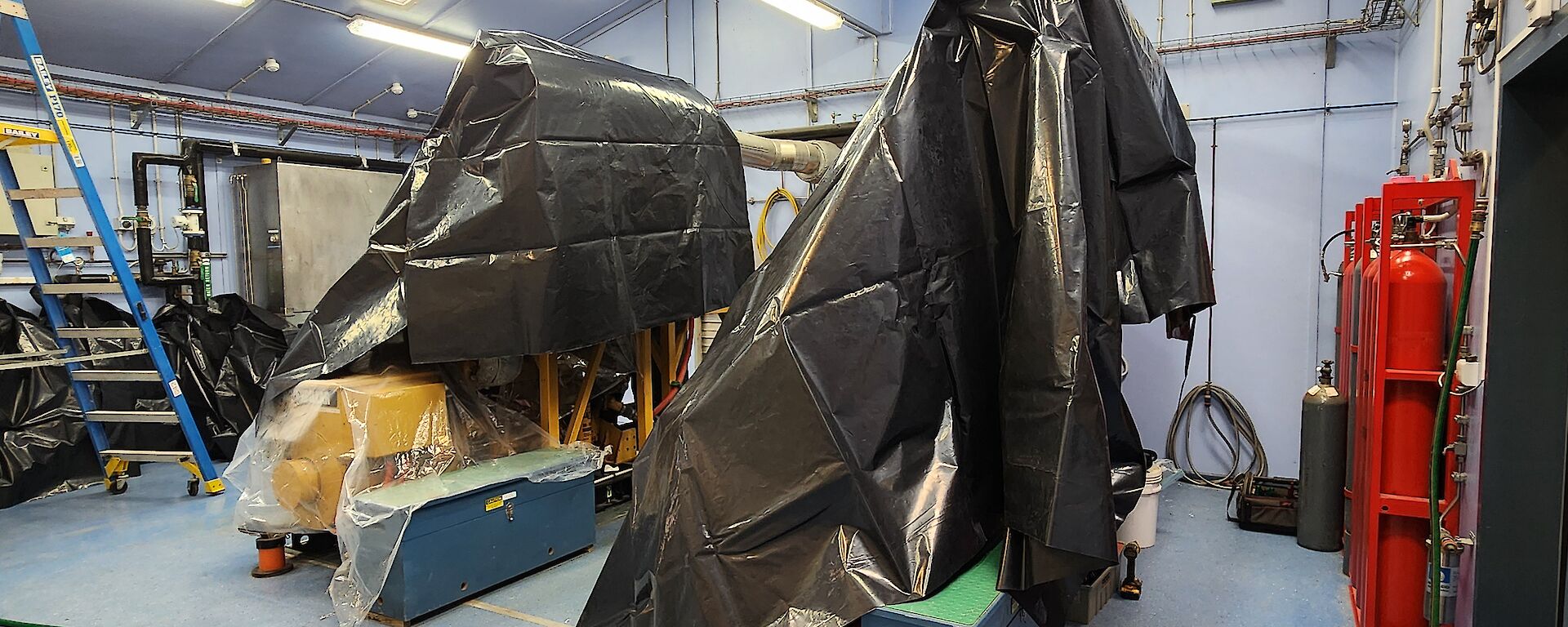 Two large machines in a blue room with black bags covering them in preparation for work