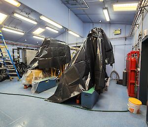 Two large machines in a blue room with black bags covering them in preparation for work