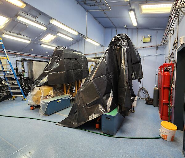 Two large machines in a blue room with black bags covering them in preparation for work