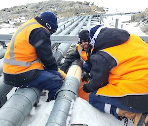 3 expeditioners working on a pipe outside